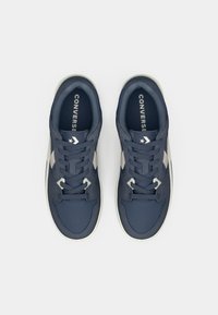 Navy blue sneakers with a smooth fabric upper, contrasting cream accents, round toe, flat laces, and a branded insole.