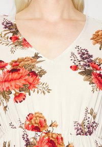Vestido com padrão floral, apresentando um decote em V, confeccionado em tecido leve. O padrão inclui flores vermelhas e roxas brilhantes com folhas verdes.