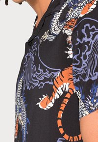 Lyhythihainen musta paita, jossa on oranssin tiikerin ja sinisen lohikäärmeen kuvio, pehmeä materiaali ja klassinen kaulus.