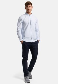 Hellblau gestreiftes Button-up-Hemd mit langen Ärmeln, kombiniert mit navyblauen Hosen und grauen Turnschuhen, im lässigen Schnitt und mit glatter Textur.