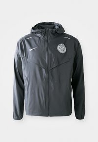 Chaqueta ligera para hombre en gris, fabricada con material resistente al agua. Cuenta con cierre de cremallera, capucha y el logo del Paris Saint-Germain en el pecho.