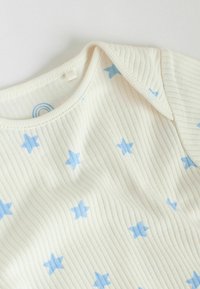 Body crème côtelé orné d'un motif d'étoiles bleues, tissu doux, encolure ronde et détails de col replié.