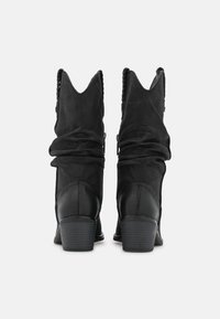 Czarne zamszowe botki za kostkę o luźnym fasonie, spiczaste noski i wplecione akcenty na górze. Zestawiony obcas i gładka tekstura dopełniają całość.