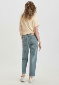 T-shirt corta gialla chiara con maniche corte, abbinata a jeans blu a vita alta. Modella che indossa sneakers bianche. Stile semplice e casual.