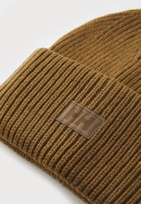 Berretto lavorato a maglia marrone con texture a coste, dotato di una toppa logo rettangolare nella stessa tonalità. Materiale morbido, vestibilità aderente.