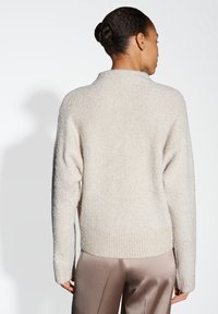 Un pull en tricot texturé beige clair avec un large col et un ourlet côtelé, doté de longues manches. Porté sur un pantalon lisse au toucher satiné.