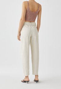 Top corto de ganchillo en rosa y púrpura, combinado con pantalones de cintura alta en color crema. Los pantalones tienen bolsillos traseros y un corte holgado.