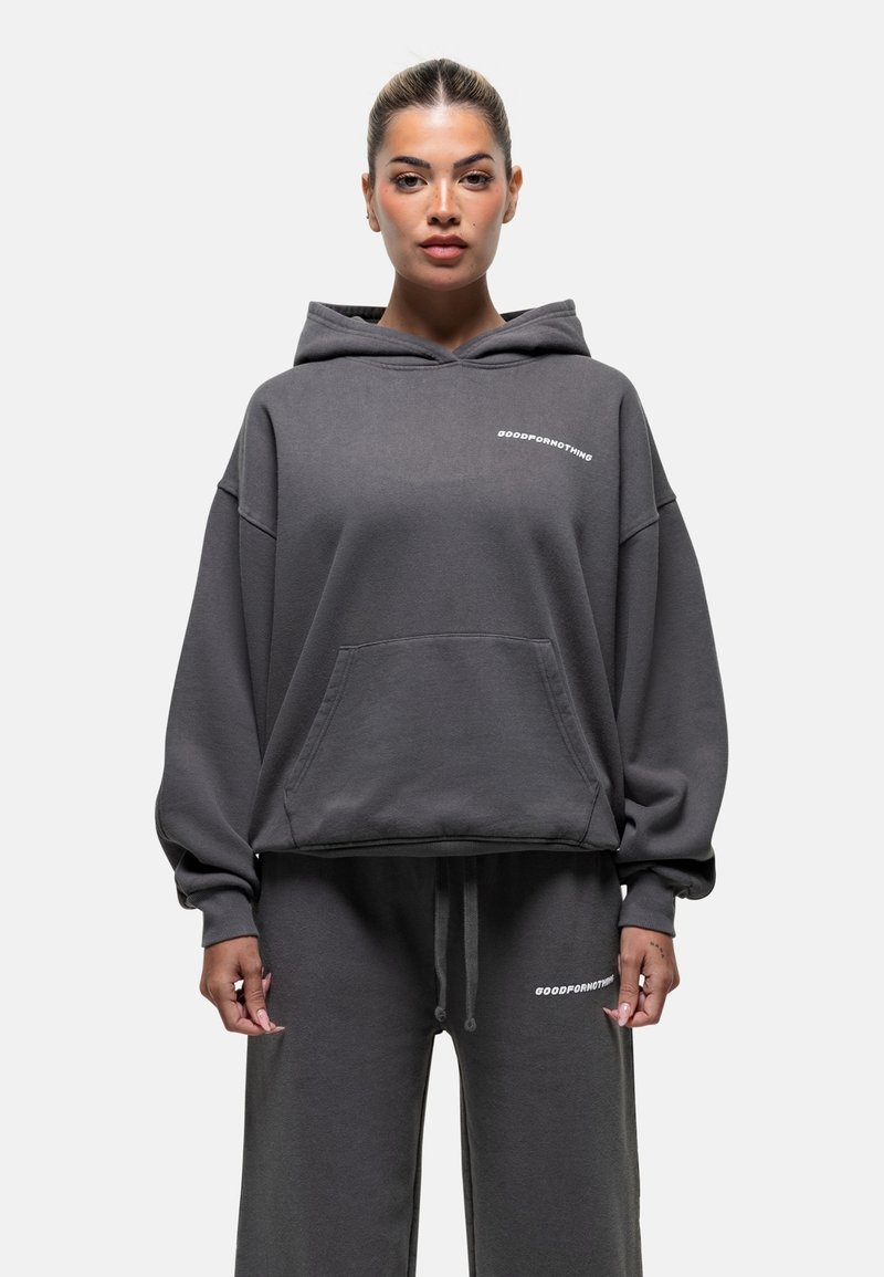 Haut à capuche surdimensionné gris en tissu doux, avec une poche avant et un logo blanc sur la poitrine, associé à un pantalon de jogging assorti.