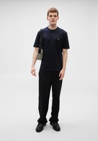 Μπλε ναυτικό t-shirt με στρογγυλή λαιμόκοψη, από βαμβακερό ύφασμα, άνετη εφαρμογή. Συνδυασμένο με μαύρο παντελόνι φαρδιάς γραμμής και μαύρα δερμάτινα παπούτσια. Διακριτική λεπτομέρεια με μικρό λογότυπο ορατή.
