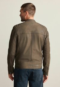 Braune Leder-Motorradjacke mit strukturierten Schulterakzenten, einer taillierten Silhouette und Reißverschlussärmeln, kombiniert mit dunklen Denim-Hosen.