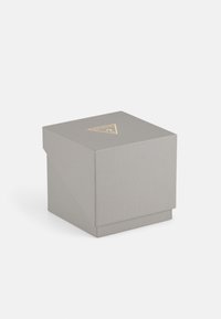 Boîte cadeau grise texturée avec un logo doré triangulaire sur le dessus. La boîte possède un rabat pliable et une base carrée.