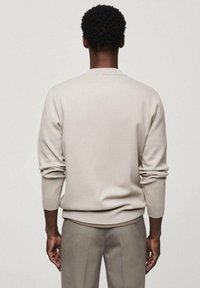 Suéter beige claro de tela suave, con cuello redondo, mangas largas y puños acanalados, combinado con pantalones a juego.