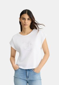 T-shirt blanc à manches courtes avec un col rond et un imprimé graphique discret au centre. Matière douce, design court, coupe décontractée.