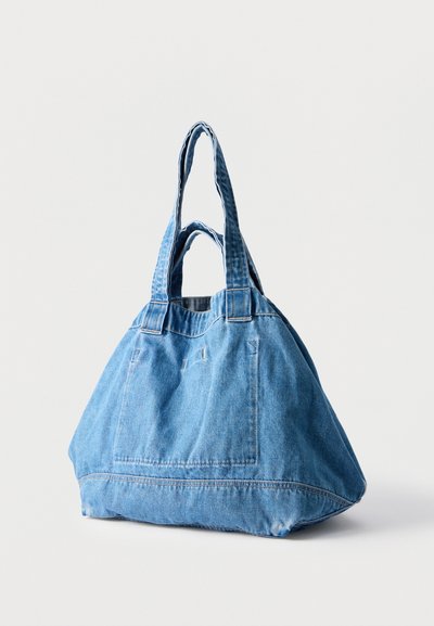 Μεγάλη τσάντα tote από μπλε τζιν με διπλές λαβές και εμφανές ράψιμο σε απλό λευκό φόντο.