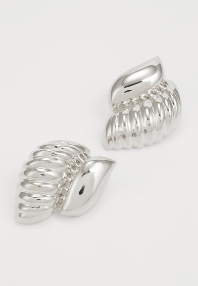 Boucles d'oreilles en métal argenté avec un design en forme de coquillage, présentant une texture striée et des accents lisses, mettant en valeur une surface réfléchissante.