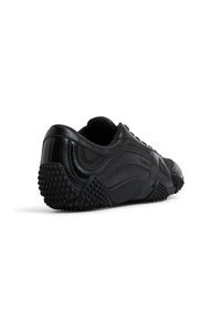 Zapatilla deportiva negra, con parte superior de cuero suave, acentos texturizados y suela de goma con un patrón de puntos para mayor agarre.