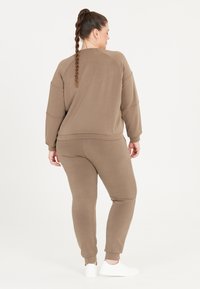 Brun loungewear-set bestående av en avslappnad långärmad sweatshirt och avslappnade joggers, kombinerad med vita sneakers. Slät textur.