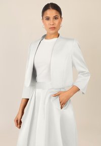 Biała skórzana kurtka z okrągłym kołnierzem, rękawami o długości trzech czwartych i eleganckim fasonem, zestawiona z dopasowaną plisowaną spódnicą.