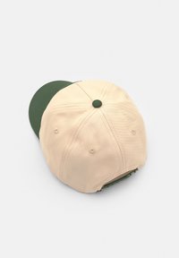 Căciulă bej cu o vizieră verde, realizată dintr-un material texturat, având patru găuri de ventilație și un nasture din același material în partea de sus.