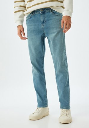 Vaqueros de mezclilla azul claro con corte recto, diseño de cinco bolsillos y detalles de costura visibles, combinados con zapatillas blancas.