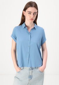 Light blue, short-sleeved blouse with a button-up front and a pointed collar. Smooth texture, relaxed fit, and rolled sleeve cuffs.