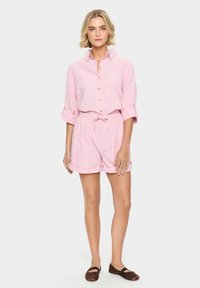 Camicia button-up rosa con maniche arrotolate, abbinata a pantaloni corti coordinati con vita regolabile a coulisse, texture liscia e vestibilità casual.