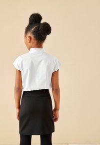 Blouse blanche à manches courtes avec un col, associée à une jupe noire. La tenue a une coupe ajustée et est faite d'un tissu léger et lisse.