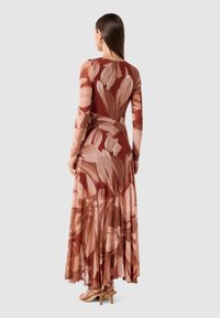 Dlouhá, přiléhavá šaty vyrobená z hladkého materiálu s velkými, abstraktními květinovými vzory v teplých odstínech rezavé a jemně růžové, s dlouhými rukávy a splývavou sukní.