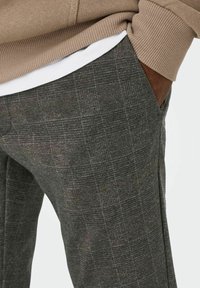 Grijze patroongedragen broek van textuurstof. Heeft een geruit design met een zak en een bruine leren accent op de taille.