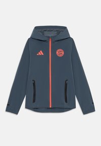 Giacca leggera blu navy con cappuccio; presenta una zip frontale arancione, tasche con zip nere e un logo del Bayern Monaco sul petto.