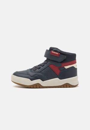 Baskets montantes en cuir navy avec des accents rouges, sangle velcro et semelle en caoutchouc blanc dotée d'une texture antidérapante et de détails perforés.