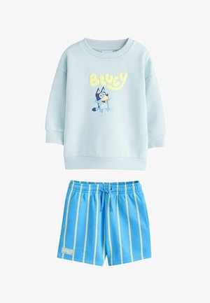 Šviesiai mėlynas džemperis ilgomis rankovėmis su „Bluey“ šuns paveikslėliu ir derančios mėlynos kelnaitės su geltonomis vertikaliomis juostomis bei raišteliu liemenėje.