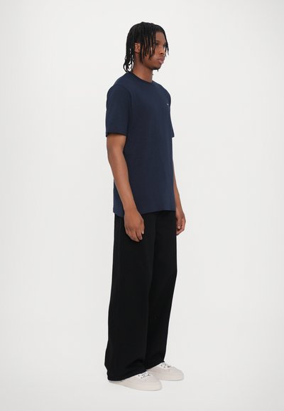 Mørkeblå bomuld t-shirt med korte ærmer, parret med løstsiddende sorte bukser og hvide sneakers. Enkel design, minimale detaljer.