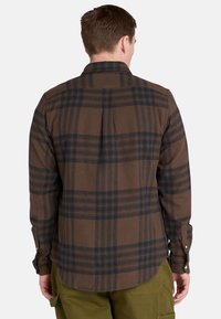 Bruine geruite flanellen shirt met zwarte checks, lange mouwen en knoopmanchetten. Getailleerde pasvorm met een rugplooien voor bewegingsvrijheid.