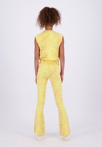Gelbes Zweiteiler-Outfit mit einem ärmellosen Oberteil und weit geschnittenen Hosen mit einem gewellten Streifenmuster. Das Material wirkt weich und strukturiert.