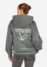 Γκρι φούτερ με κουκούλα και κορδόνι, που διαθέτει λευκό γραφικό σχέδιο ενός βάζου με λουλούδια και κείμενο στην πλάτη. Ριμπ μανσέτες και στρίφωμα.