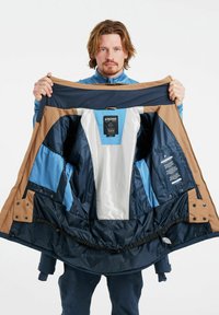 Chaqueta de esquí con una capa exterior marrón. El interior presenta paneles azules y forro de malla, con múltiples bolsillos y material impermeable.