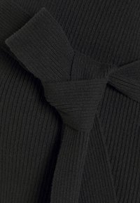 Czarna dzianina prążkowana z dekoracyjnym wiązanym kokardą. Tekstura jest miękka i lekko elastyczna, co nadaje jej uporządkowany wygląd.