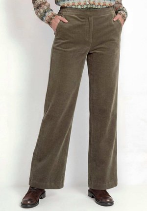 Cordweite-Hose in Olivgrün, getragen mit Händen in den Taschen und braunen Lederschuhen.