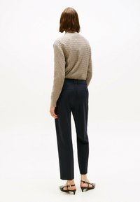 Beige gestructureerde trui, marineblauwe op maat gemaakte broek en zwarte hakschoenen. Weergave van de achterkant die de pasvorm en ontwerpdetails laat zien.