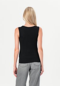 Black sleeveless top with a round neckline, made of smooth fabric. Paired with light gray wide-leg jeans featuring back pockets and seams.