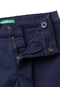 Pantalones de algodón azul marino con cremallera en la bragueta, cierre de botón de metal y etiqueta verde. Presentan detalles de costura y una textura suave.