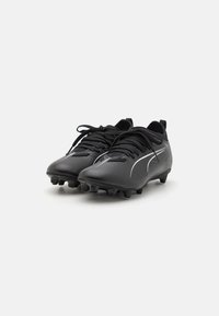 Botas de fútbol negras con una superficie texturizada, acentos blancos y un diseño con cordones. Equipadas con tacos moldeados para mayor tracción.