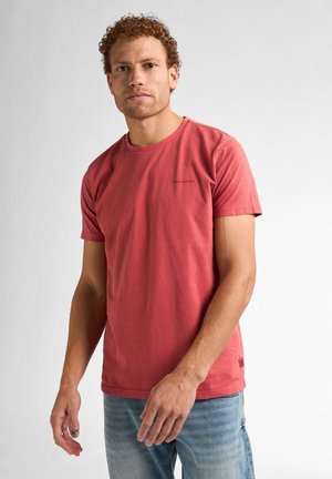 Kortærmet T-shirt med rund hals i koralfarvet bomuld med let sømdetaille, båret med falmede blå jeans. Minimalistisk branding på brystet.