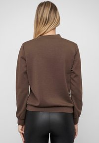 Brauner Sweatshirt mit Rundhalsausschnitt, langen Ärmeln und einem umgeschlagenen Saum. Hergestellt aus weichem Material, bietet es eine glatte Textur und ein einfaches Design.