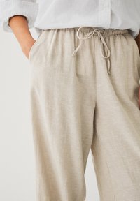 Pantalon en lin léger beige avec une taille élastique et un détail de cordon de serrage. Présente des poches latérales et une coupe décontractée à jambe large.