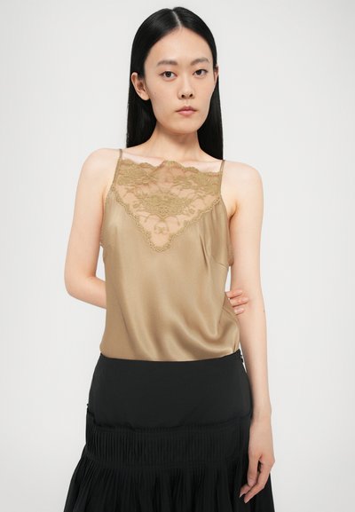 Beige satin camisole, jossa on läpikuultava pitsireunus kaula-aukossa, ohuet hihnat ja sileä pinta. Yhdistetty mustaan hameeseen.