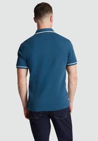 Le polo est de couleur bleu foncé unie avec des accents blancs le long du col et des manches, confectionné en tissu doux et respirant.