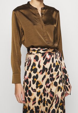 Person iført en skinnende brun bluse med lange ærmer stoppet ned i en beige, sort og lyserød abstrakt leopardprint nederdel med taljebånd.