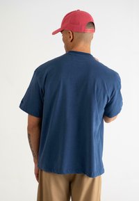 Marineblå bomulds t-shirt med korte ærmer, rund halsudskæring og afslappet pasform; båret med en lyserød baseballkasket. Simpelt design, uden mønstre.